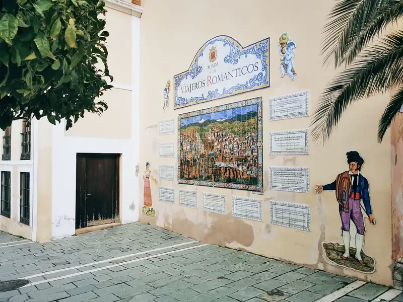 Spanish wall with mosaic art depicting travelers and historical scenes in an urban setting.