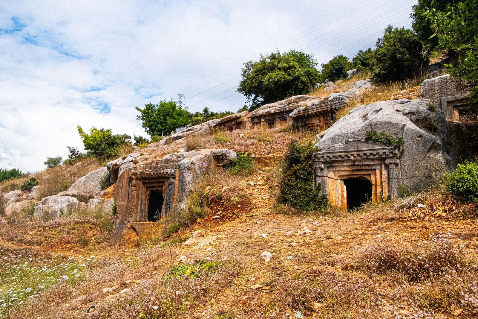 Explore ancient rock-cut tombs nestled in a scenic hillside landscape, captured brilliantly under a clear sky.
