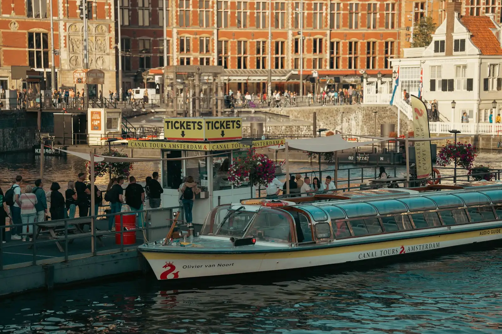 Busy canal tour dock in Amsterdam with people waiting and a boat ready for departure.
