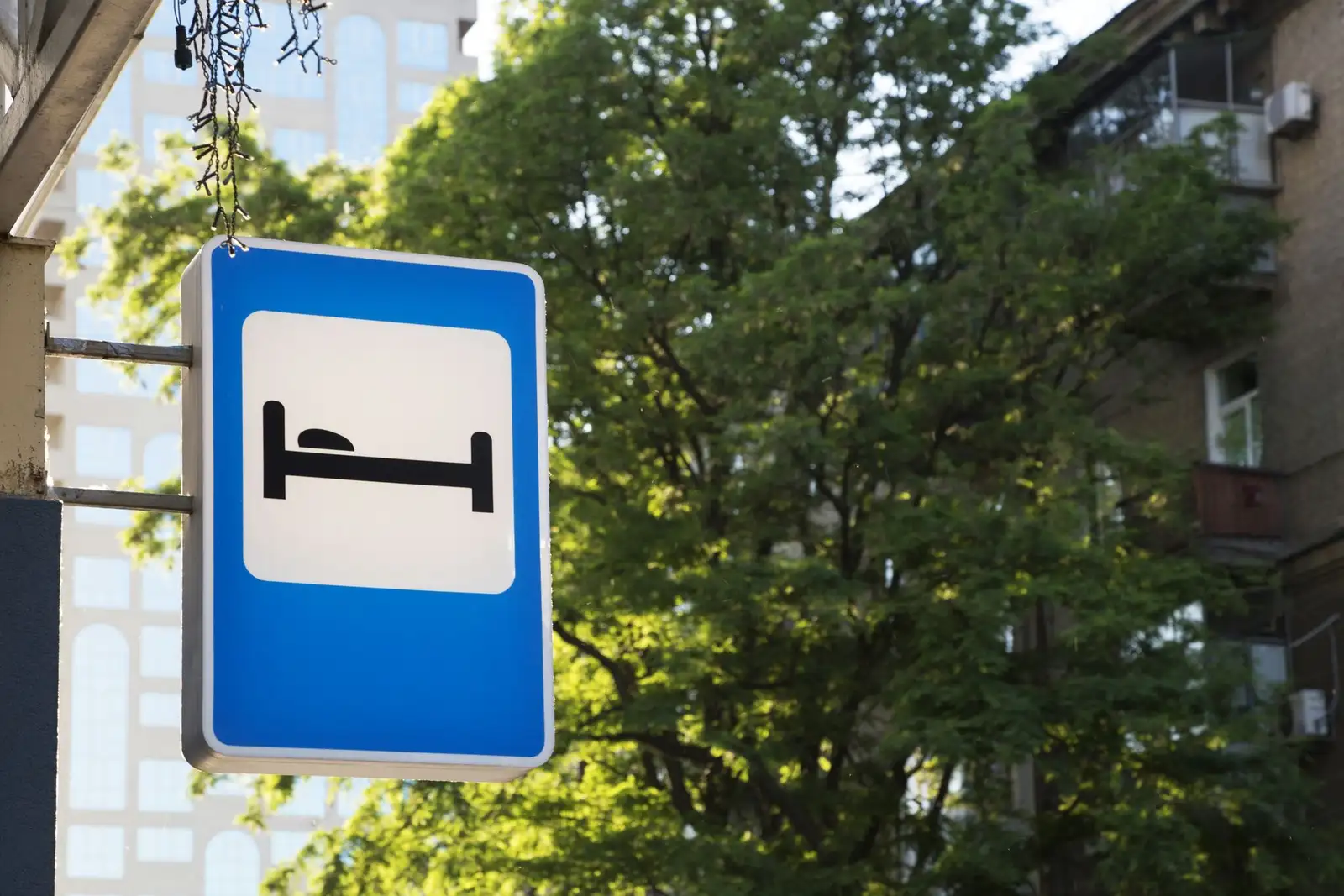 Hotel sign with bed symbol amidst urban greenery and buildings.