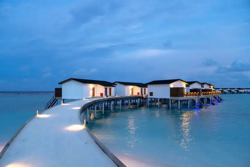 Stunning overwater bungalows lit up at twilight, providing a serene tropical getaway.