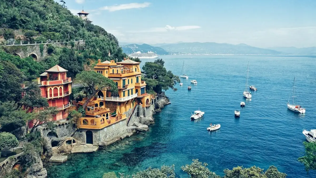Vibrant, colorful villas perched on dramatic rocky cliffs, overlooking the serene blue Ligurian Sea in Portofino, Italy.